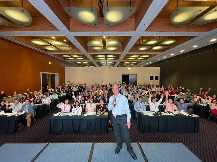 Ponente del Congreso 2025 en el escenario mientras la audiencia participa con las manos levantadas