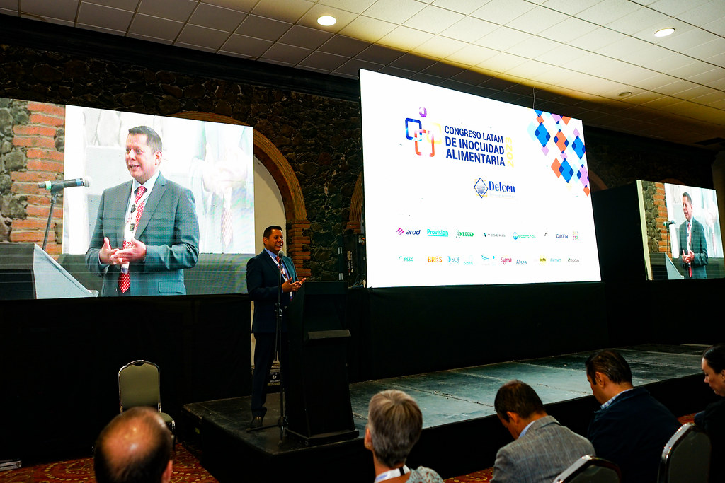 Ponente en el podio del escenario principal con la pantalla del Congreso Latam de Inocuidad Alimentaria 2023